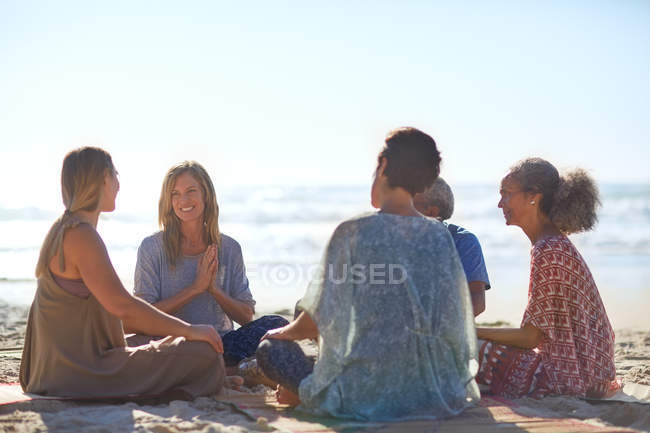 Happy friends talking in circle on sunny beach during yoga retreat — Stock Photo