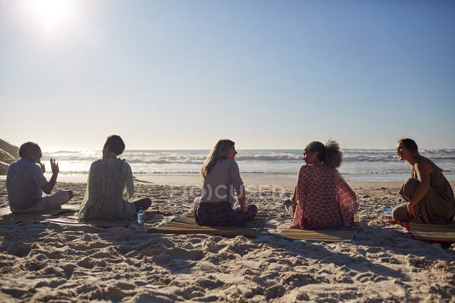 Clase de yoga hablando en la playa soleada durante el retiro de yoga - foto de stock