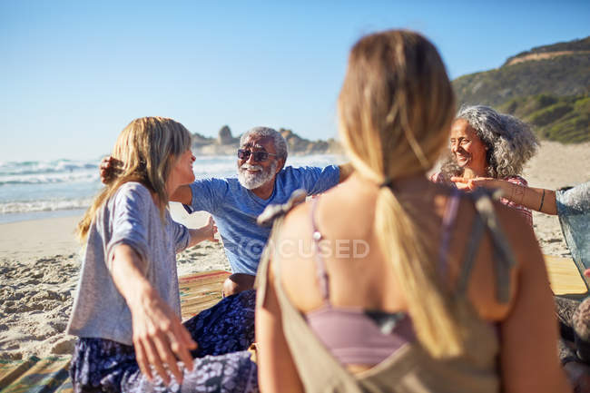 Amici che si abbracciano in cerchio sulla spiaggia soleggiata durante il ritiro yoga — Foto stock