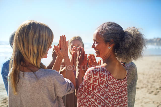 Mujeres amigas con las manos apretadas en círculo en la playa soleada durante el retiro de yoga - foto de stock