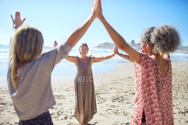 Mujeres uniendo las manos en círculo en la playa soleada durante el retiro de yoga - foto de stock