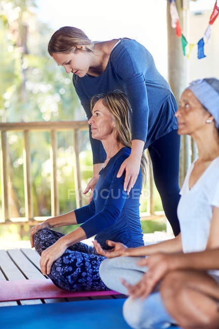Инструктор-женщина регулирует плечи студентов во время занятий йогой — стоковое фото