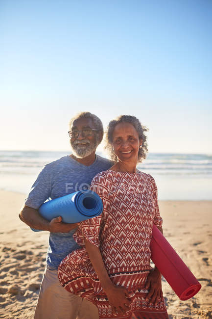 Portrait happy senior couple with yoga mats on sunny beach — Stock Photo