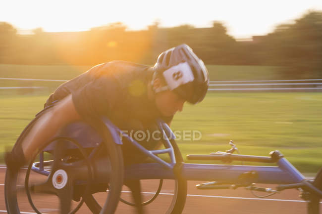 Jeune athlète paraplégique déterminée à accélérer le long de la piste de sport dans une course en fauteuil roulant — Photo de stock