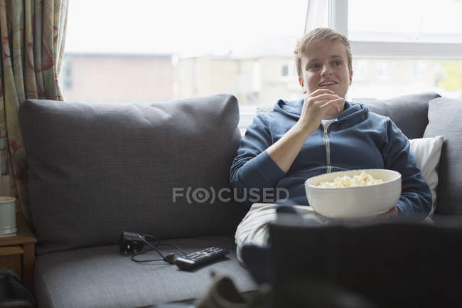 Молодая женщина ест попкорн на диване — стоковое фото