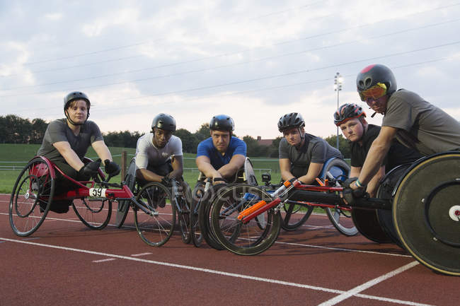 Atletas parapléjicos determinados y confiados en retratos entrenando para la carrera en silla de ruedas en pista deportiva - foto de stock