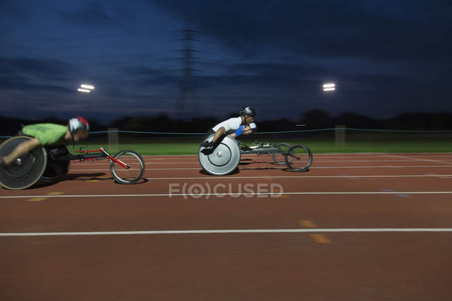 Atletas paraplégicos acelerando ao longo da pista de esportes em corrida em cadeira de rodas — Fotografia de Stock