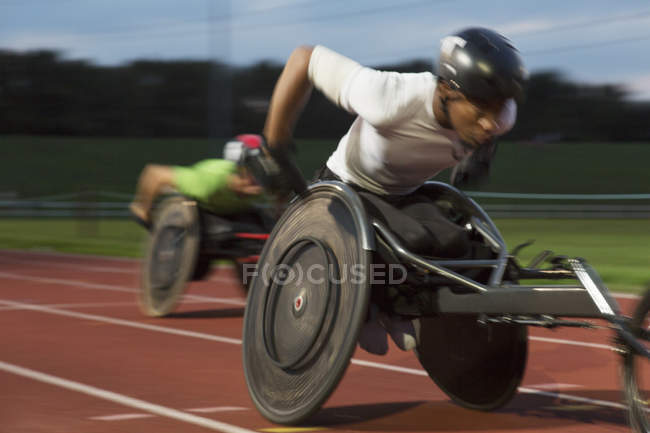 Deportista parapléjico joven decidido a correr a lo largo de la pista deportiva en la carrera en silla de ruedas - foto de stock