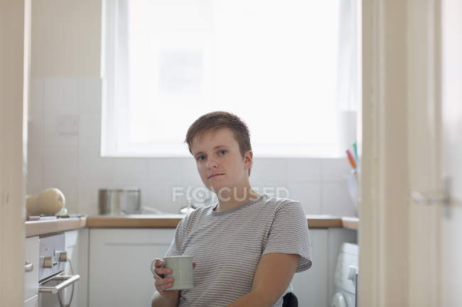 Retrato confiante jovem mulher em cadeira de rodas beber café na cozinha apartamento — Fotografia de Stock
