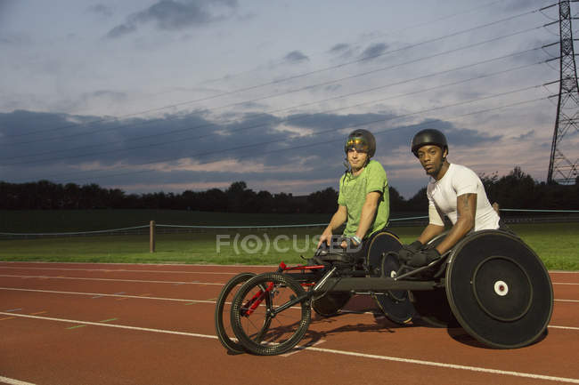 Портрет уверенный парализованные спортсмены подготовка к гонке на инвалидных колясках на спортивной трассе ночью — стоковое фото