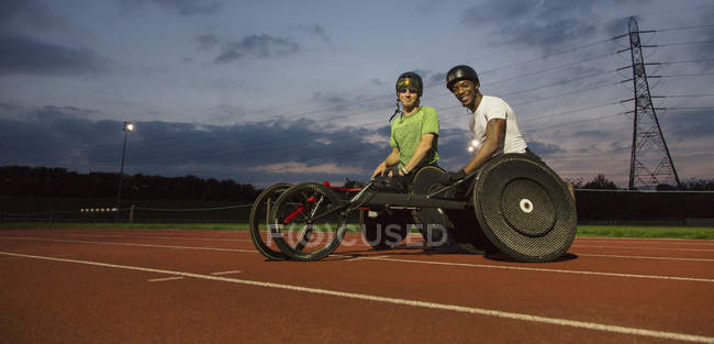 Retrato confiante, atletas paraplégicos em pista de esportes, treinamento para corrida em cadeira de rodas à noite — Fotografia de Stock