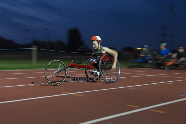 Atleta paraplégico adolescente acelerando ao longo da pista de esportes em corrida em cadeira de rodas — Fotografia de Stock