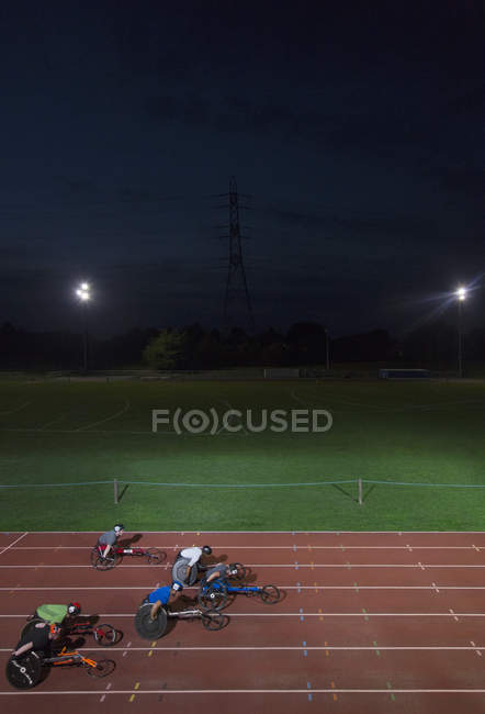 Паралімпійські спортсмени прискорюються вздовж спортивної траси в гонці на інвалідних візках вночі — стокове фото