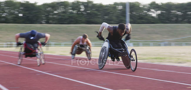 Atletas paraplégicos acelerando ao longo da pista de esportes em corrida em cadeira de rodas — Fotografia de Stock