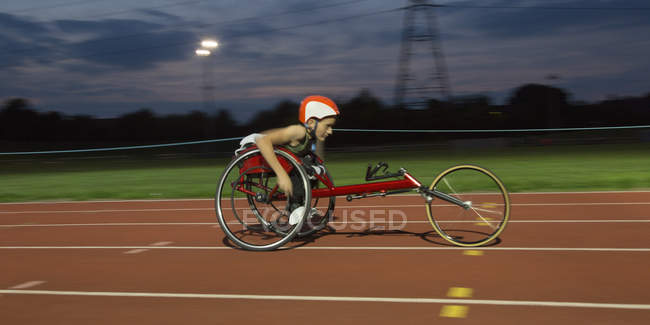 Determinado adolescente parapléjico atleta exceso de velocidad a lo largo de pista deportiva en la carrera en silla de ruedas - foto de stock