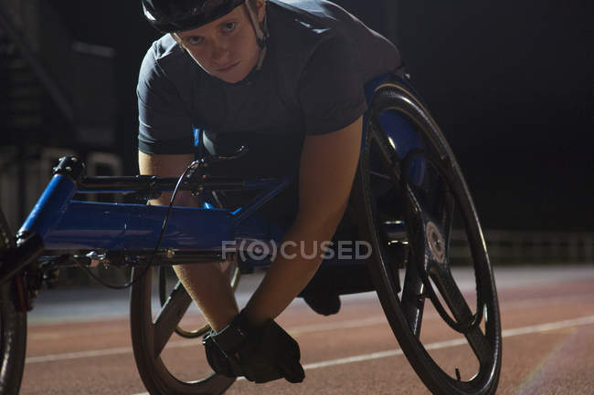 Portrait determined young female paraplegic athlete training for wheelchair race on sports track at night — Stock Photo
