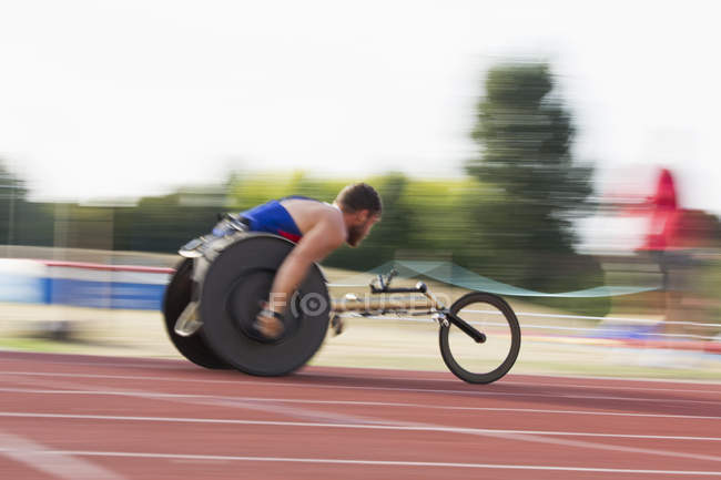 Determinato giovane atleta paraplegico maschile che corre lungo la pista sportiva in gara su sedia a rotelle — Foto stock