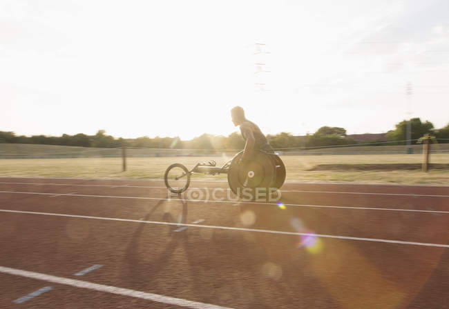 Jeune athlète masculin paraplégique s'entraînant pour la course en fauteuil roulant sur piste de sport ensoleillée — Photo de stock