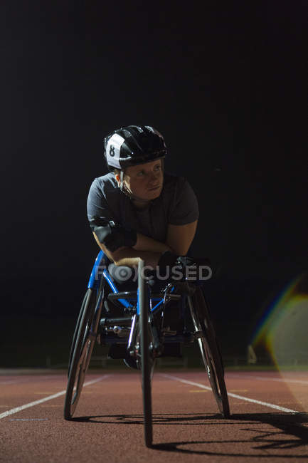 Jeune athlète paraplégique déterminée s'entraînant pour la course en fauteuil roulant sur piste de sport la nuit — Photo de stock