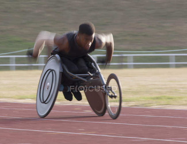 Jeune athlète paraplégique masculin déterminé à accélérer le long de la piste de sport pendant la course en fauteuil roulant — Photo de stock