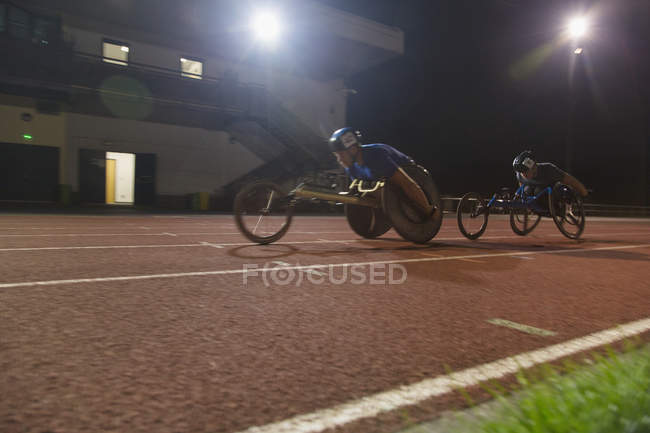 Паралімпійські спортсмени прискорюються вздовж спортивної траси в гонці на інвалідних візках вночі — стокове фото