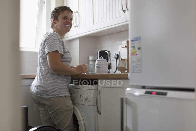 Усміхнена молода жінка готує чай на кухні квартири — стокове фото