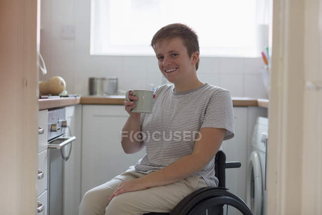 Porträt lächelt, selbstbewusste junge Frau im Rollstuhl trinkt Tee in Wohnküche — Stockfoto