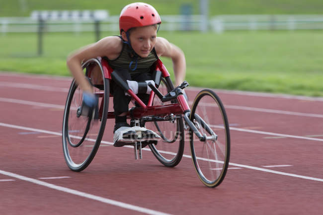 Decidido, duro adolescente atleta parapléjico exceso de velocidad a lo largo de pista deportiva en la carrera en silla de ruedas - foto de stock