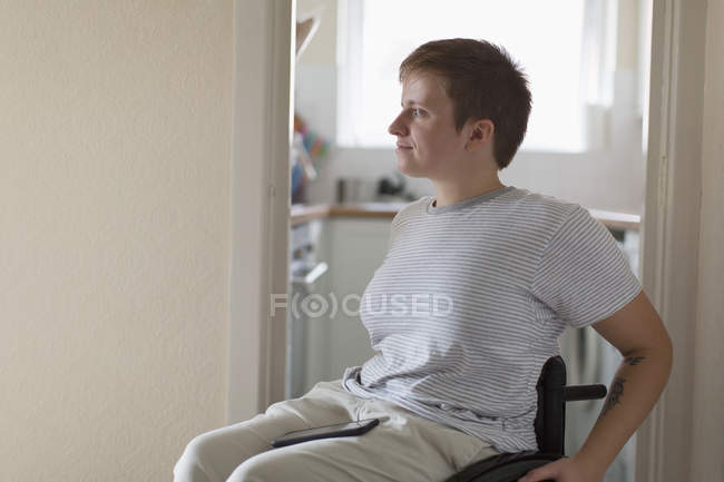 Jeune femme réfléchie en fauteuil roulant à la maison — Photo de stock