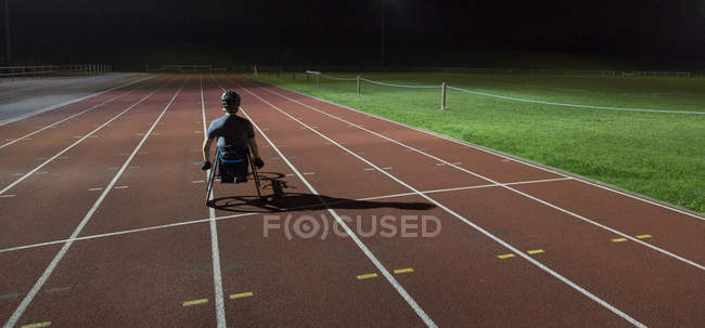 Entrenamiento de atleta parapléjico para la carrera en silla de ruedas en pista deportiva por la noche - foto de stock