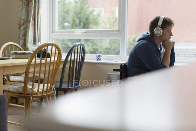 Serena giovane donna sulla sedia a rotelle che ascolta musica con le cuffie alla finestra — Foto stock