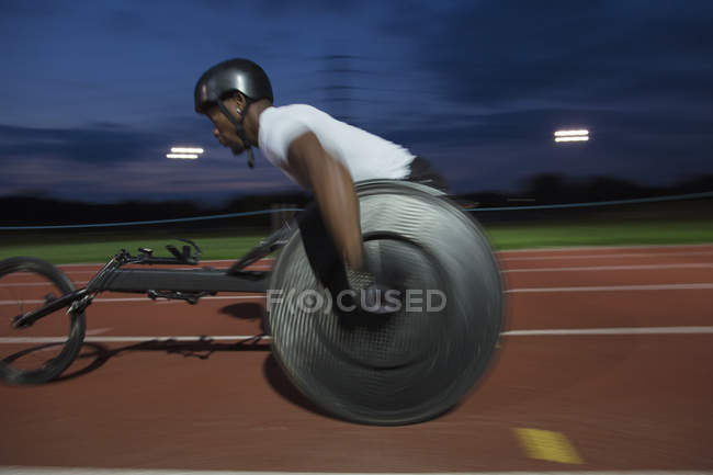 Решительный молодой парализованный спортсмен, мчащийся по спортивной трассе в гонке на инвалидных колясках ночью — стоковое фото
