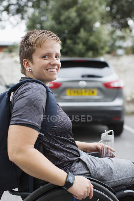 Retrato confiante jovem estudante universitário em cadeira de rodas no estacionamento — Fotografia de Stock