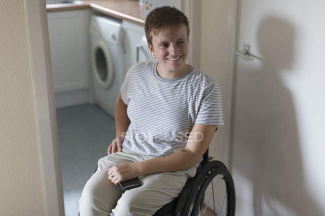 Mujer joven sonriente en silla de ruedas en casa - foto de stock