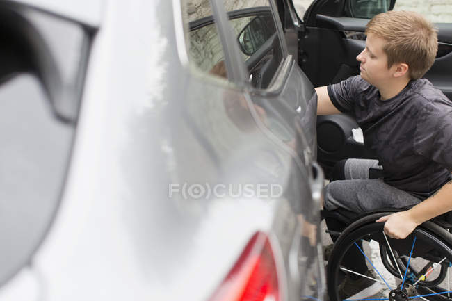 Mujer joven en silla de ruedas abriendo la puerta del coche - foto de stock