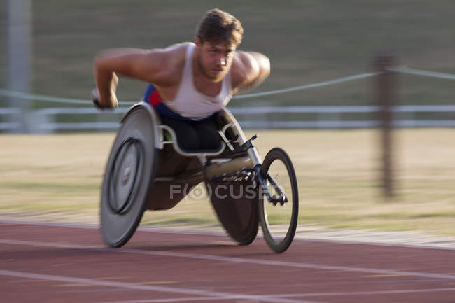 Determinado jovem atleta paraplégico do sexo masculino acelerando ao longo da pista de esportes na corrida em cadeira de rodas — Fotografia de Stock