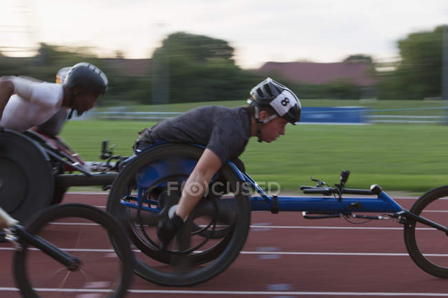Atletas paraplégicos determinados acelerando ao longo da pista de esportes em corrida em cadeira de rodas — Fotografia de Stock