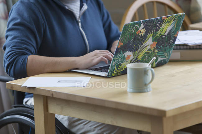 Молода жінка в інвалідному візку використовує ноутбук за столом — стокове фото