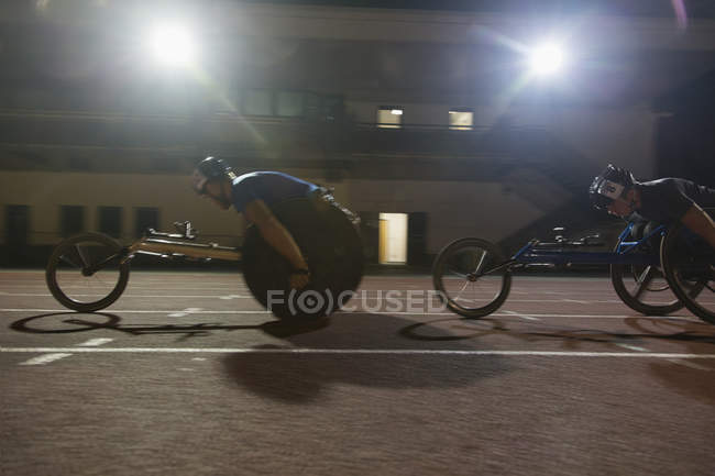 Atleta paraplégico acelerando ao longo da pista de esportes durante a corrida em cadeira de rodas — Fotografia de Stock