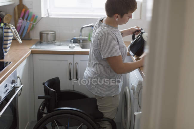 Jeune femme avec fauteuil roulant verser le thé dans la cuisine de l'appartement — Photo de stock