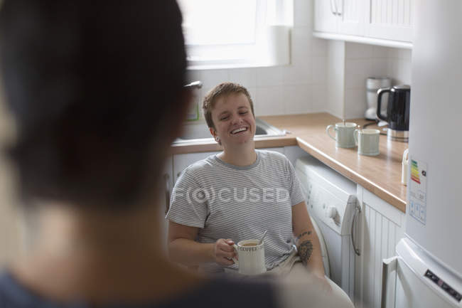 Jovem feliz na cadeira de rodas bebendo chá na cozinha do apartamento — Fotografia de Stock