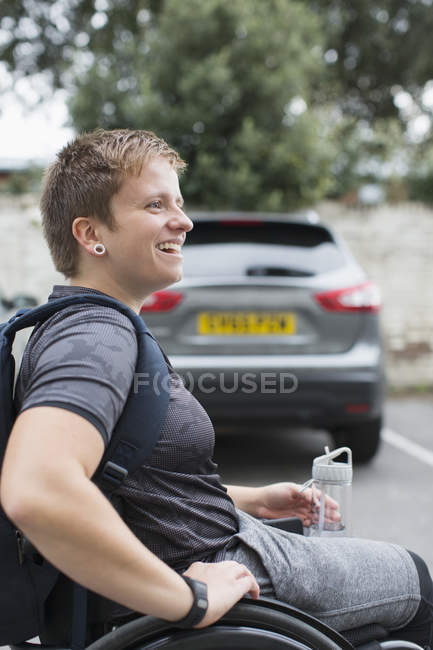 Happy young female university student in wheelchair in parking lot — Stock Photo