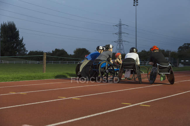 Paraplegic athletes huddling on sports track, training for wheelchair race at night — Stock Photo