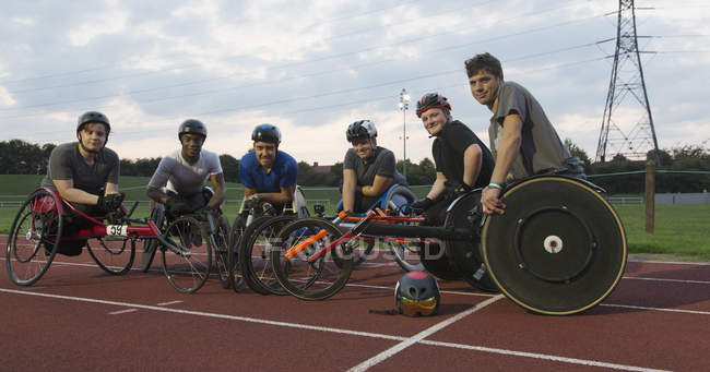 Entrenamiento de atletas parapléjicos confiados en retratos para carreras en silla de ruedas en pista deportiva - foto de stock