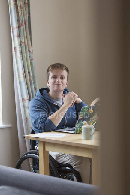 Portrait confident young woman in wheelchair using laptop at dining table — Stock Photo