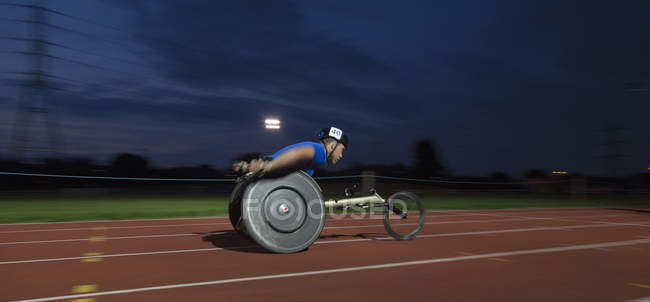 Молодий чоловічий паралеліст, що перевищує швидкість вздовж спортивної траси в гонці на інвалідних візках вночі — стокове фото