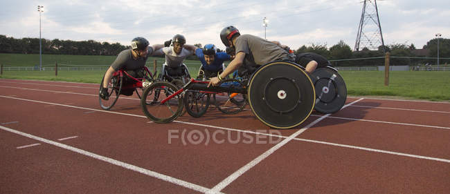 Atleti paraplegici determinati che si uniscono in un abbraccio, allenamento per la corsa in sedia a rotelle su pista sportiva — Foto stock