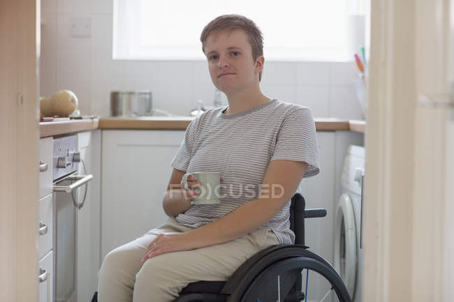 Ritratto fiduciosa giovane donna in sedia a rotelle bere il tè in cucina appartamento — Foto stock