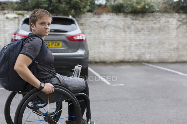 Retrato confiante jovem estudante universitário em cadeira de rodas no estacionamento — Fotografia de Stock