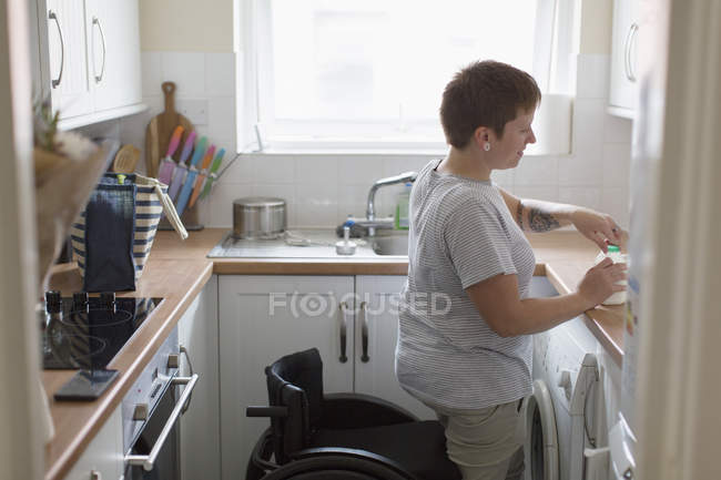 Jeune femme avec fauteuil roulant dans la cuisine appartement — Photo de stock